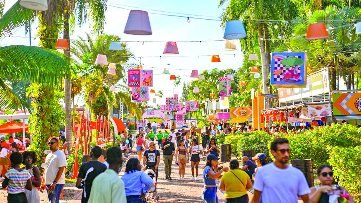 Visitantes disfrutan de Bite Food Fest en un espacio al aire libre decorado con luces, lámparas de colores, vegetación tropical y puestos de comida.