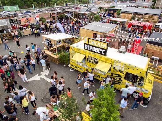 Vista aérea de un festival gastronómico al aire libre con numerosos visitantes recorriendo puestos de comida, camiones de comida y pequeños stands decorados. En primer plano destaca un camión amarillo de Chicken Republic, rodeado de personas que hacen fila y disfrutan del evento.